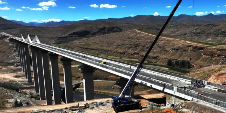 A long concrete bridge spans a river valley in the Mokhotlong highlands of Lesotho, with dignitaries gathered for an official opening ceremony.