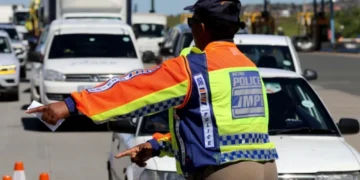 A traffic officer at a roadside checkpoint writing out an infringement notice for a driver in South Africa