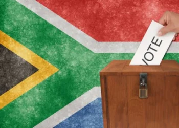 A voter placing a folded ballot paper into a sealed ballot box at a South African voting station