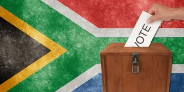 A voter placing a folded ballot paper into a sealed ballot box at a South African voting station