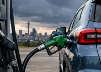 A fuel attendant filling a car at a South African petrol station with the price board visible behind
