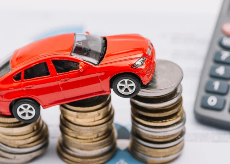 A customer signing a vehicle finance agreement at a dealership desk with a new car in the showroom behind