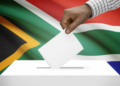 A voter marks a ballot paper behind a cardboard voting booth at a South African voting station