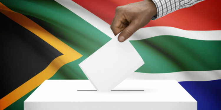 A voter marks a ballot paper behind a cardboard voting booth at a South African voting station
