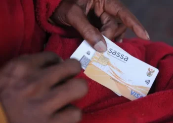 A queue of grant beneficiaries waiting outside a SASSA local office with identity documents in hand