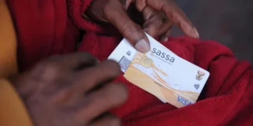 A queue of grant beneficiaries waiting outside a SASSA local office with identity documents in hand