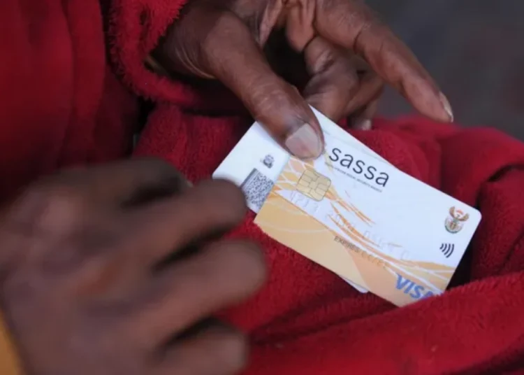 A queue of grant beneficiaries waiting outside a SASSA local office with identity documents in hand
