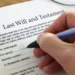 Hand signing a printed last will and testament at a desk while two witnesses look on