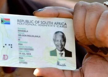 A Home Affairs official handing a Smart ID card to a young applicant at a service counter